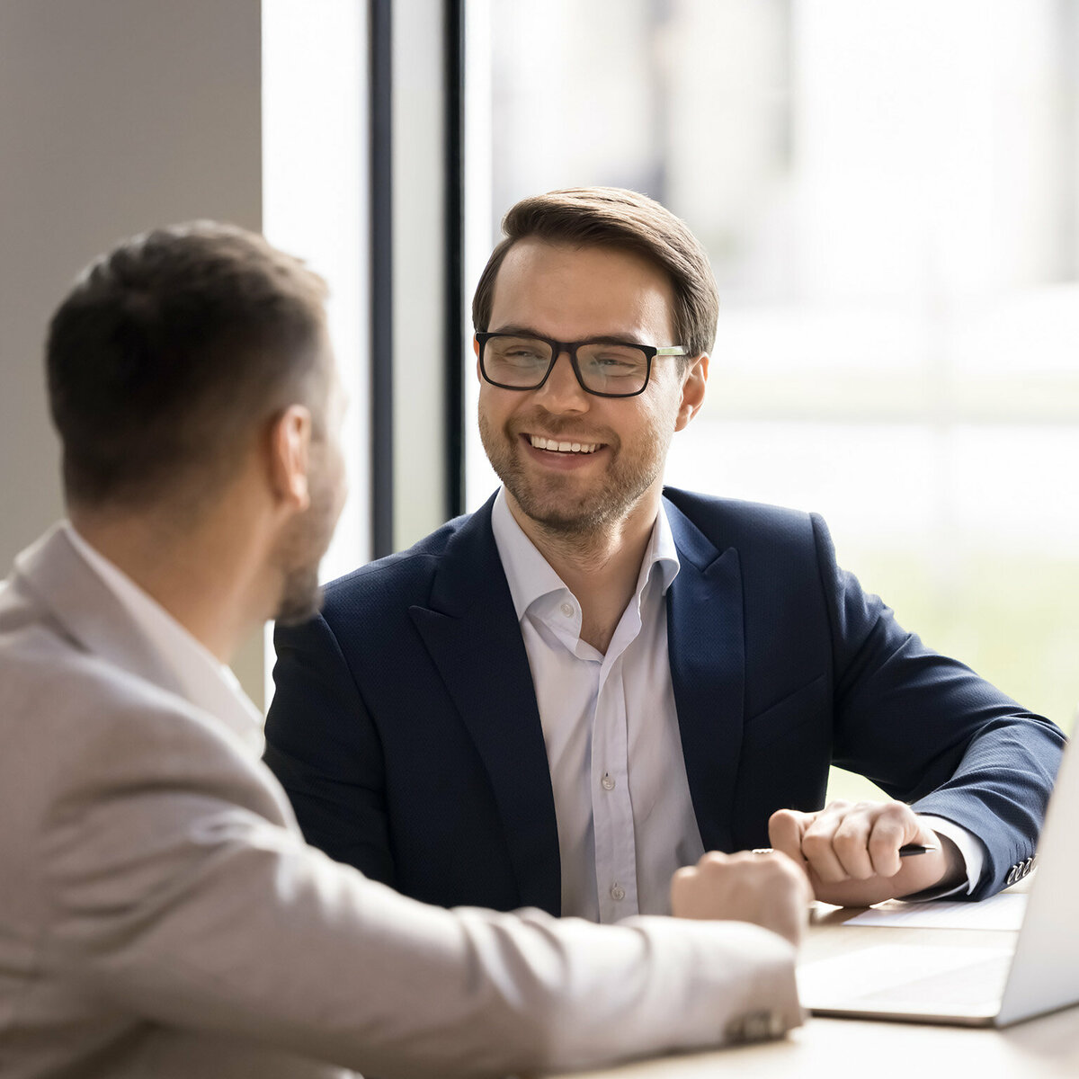 A business man is sitting with his client at a table with his laptop open.